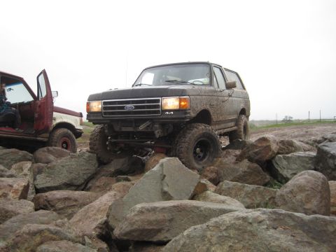 1989 Ford Bronco - Two Ford Broncos navigate a rocky, off-road course under an overcast sky.