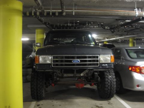 1989 Ford Bronco - A dark gray Ford Bronco is parked in a garage, showing its front end and lifted suspension.