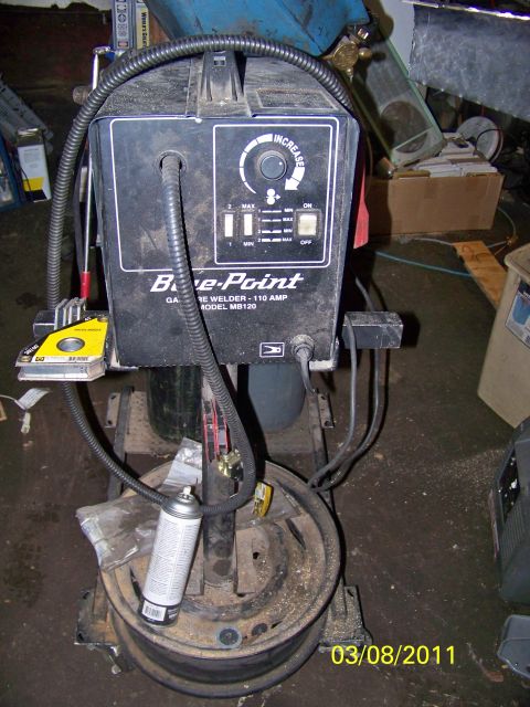 1989 Ford Bronco - A Bare-Point wire welder is shown on a stand, with a spray can and a wheel rim visible.
