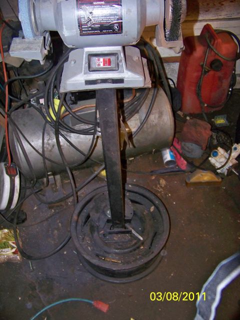 1989 Ford Bronco - A bench grinder is mounted on a stand that has a wheel rim as its base, surrounded by various tools and equipment.