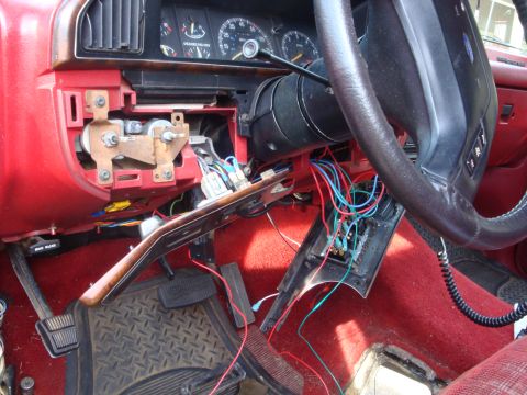 1989 Ford Bronco - The dashboard and steering column of a vehicle are shown with many wires exposed and disconnected, indicating repair or modification work.