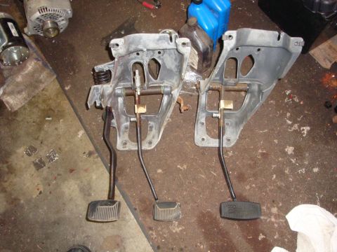 1989 Ford Bronco - Two sets of vehicle pedal assemblies are shown, likely for a manual transmission vehicle, resting on a cluttered garage floor.