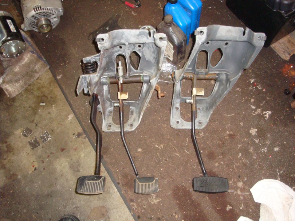 Two vehicle pedal assemblies with brake and clutch pedals, lying on a workshop floor
