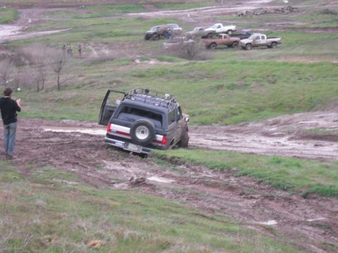1991 Ford Bronco - A 1991 Ford Bronco navigates a muddy off-road course, with other vehicles visible in the background.