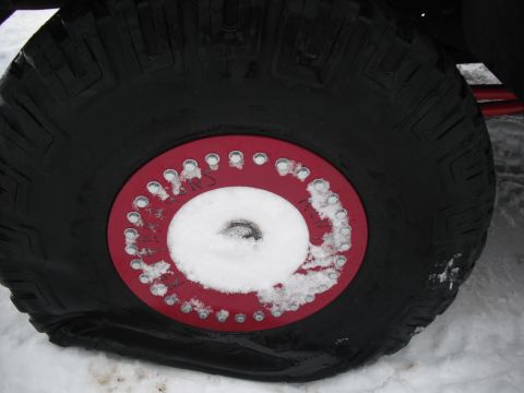 1991 Ford Bronco - A close-up view of a tire and red beadlock ring, covered in snow, suggesting off-road use in winter conditions.