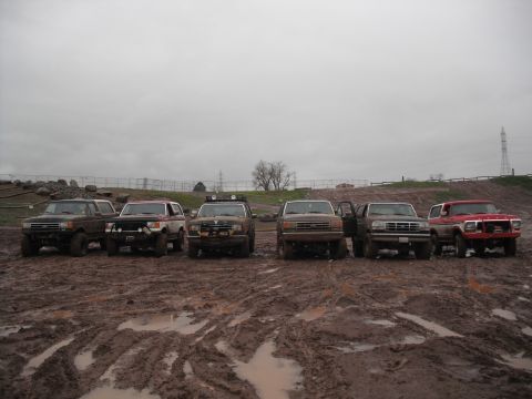1991 Ford Bronco - Several trucks and SUVs are lined up in a very muddy area with tire tracks visible.