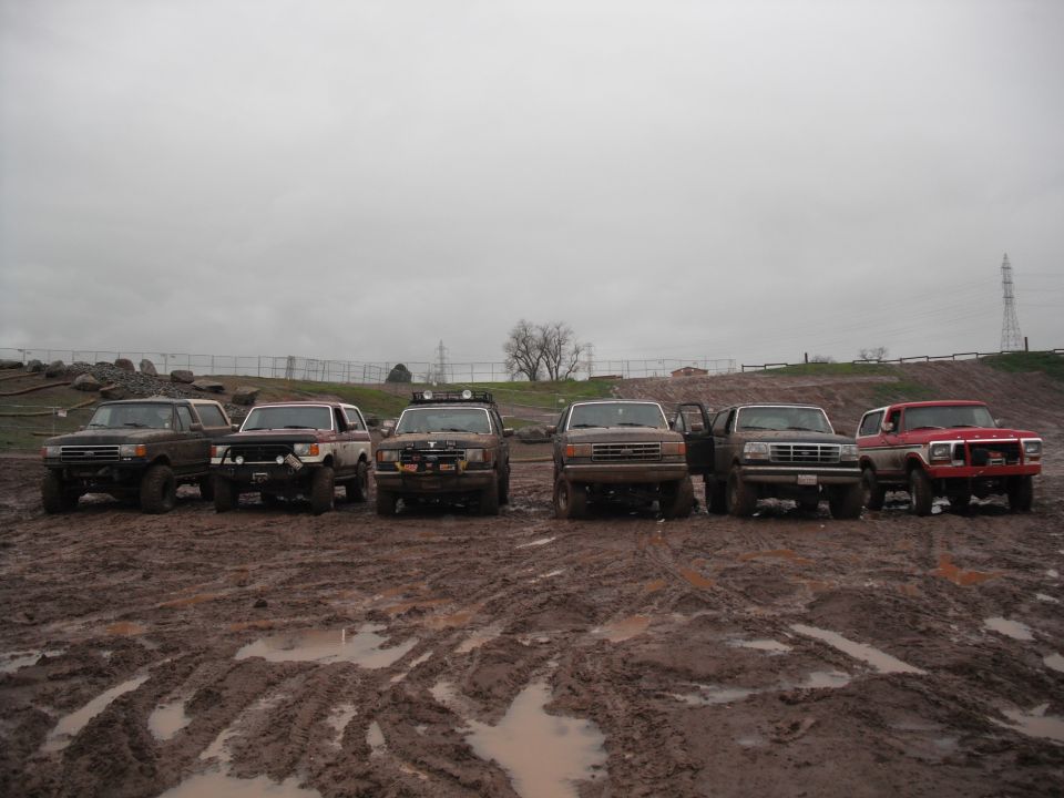 Six off-road vehicles parked in a muddy field under a cloudy sky