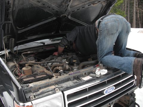 1991 Ford Bronco - A person works on the engine of a 1991 Ford Bronco, with the hood open and the Ford logo visible on the grille.