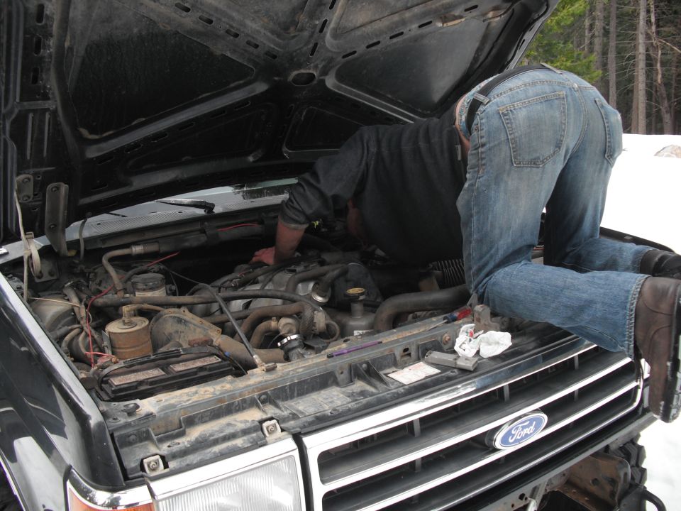 1991 Ford Bronco engine bay with a person working on the engine. The Ford logo is visible on the grille