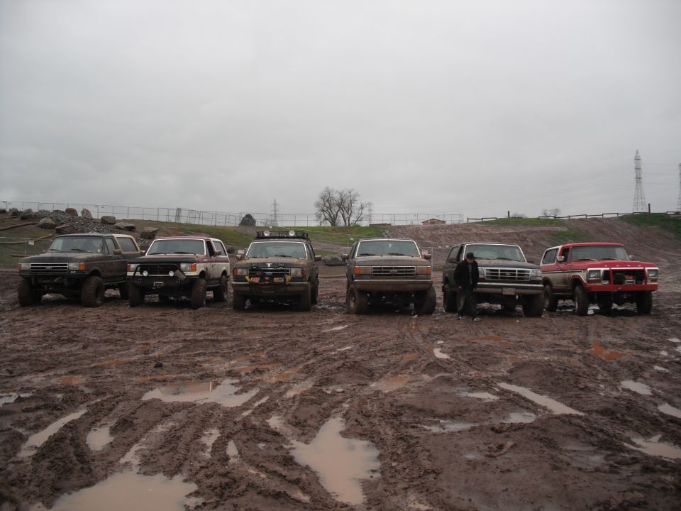 Six Ford Broncos in a row, front view, muddy conditions. One is red