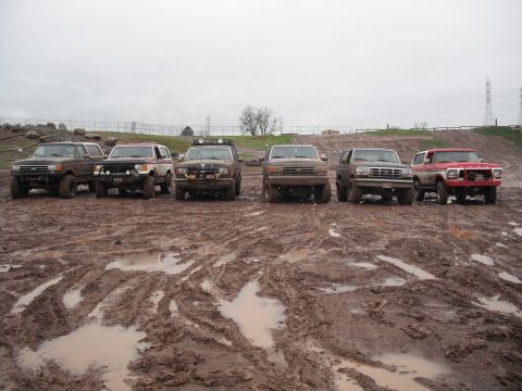 1991 Ford Bronco - Several off-road vehicles are lined up in a muddy, wet terrain, suggesting a recent off-road event or challenging driving conditions.