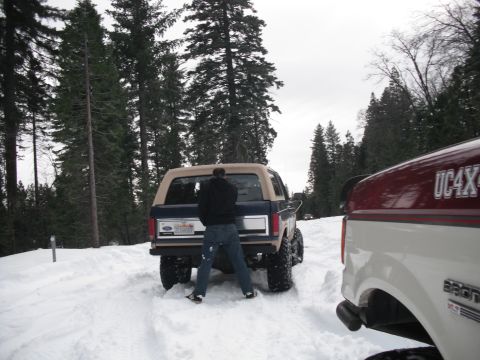 1991 Ford Bronco - A blue Ford Bronco is parked in the snow with a person standing behind it, while another truck is partially visible on the right.