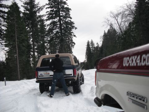 1991 Ford Bronco - A 1991 Ford Bronco is seen from the rear in a snowy environment, with another vehicle's text visible.