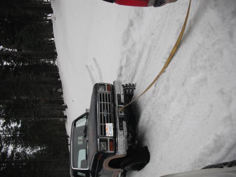 1991 Ford Bronco - A black Ford Bronco is stuck in a snowy area, with a tow strap attached to the front.