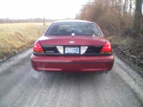 1999 Ford Crown Victoria - Rear view of a red Ford Crown Victoria on a dirt road, showing its taillights and license plate.