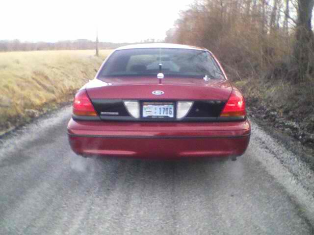 Red Ford Crown Victoria, rear view, on a dirt road. License plate 1706