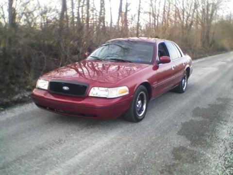 1999 Ford Crown Victoria - This red 1998 Ford Crown Victoria sedan is seen from a three-quarter front view on a gravel road with trees in the background.