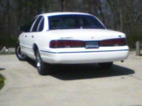 1999 Ford Crown Victoria - White sedan seen from the rear on a paved surface with trees in the background.