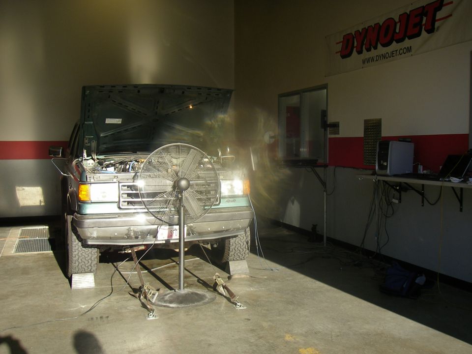 Teal Ford SUV strapped on a Dynojet chassis dyno with hood up and cooling fan in front