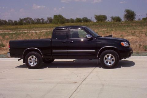 1988 Ford Bronco - Side view of a black pickup truck parked on a concrete surface with a grassy embankment in the background.