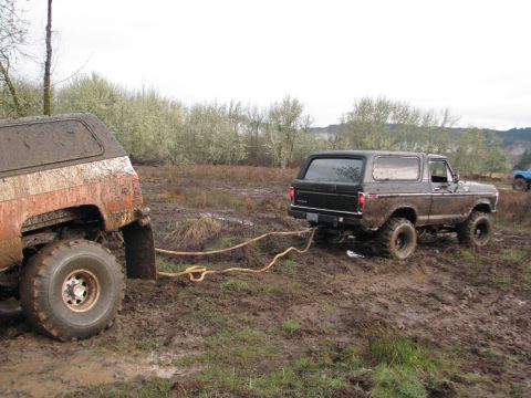 1978 Ford Bronco - Two muddy off-road vehicles are stuck in a field, with one being towed by the other.