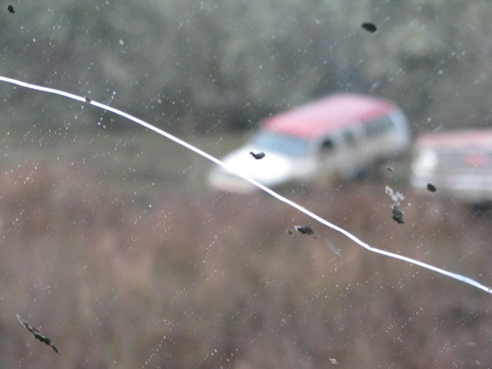 Red and white SUV seen through a cracked windshield with mud splatters