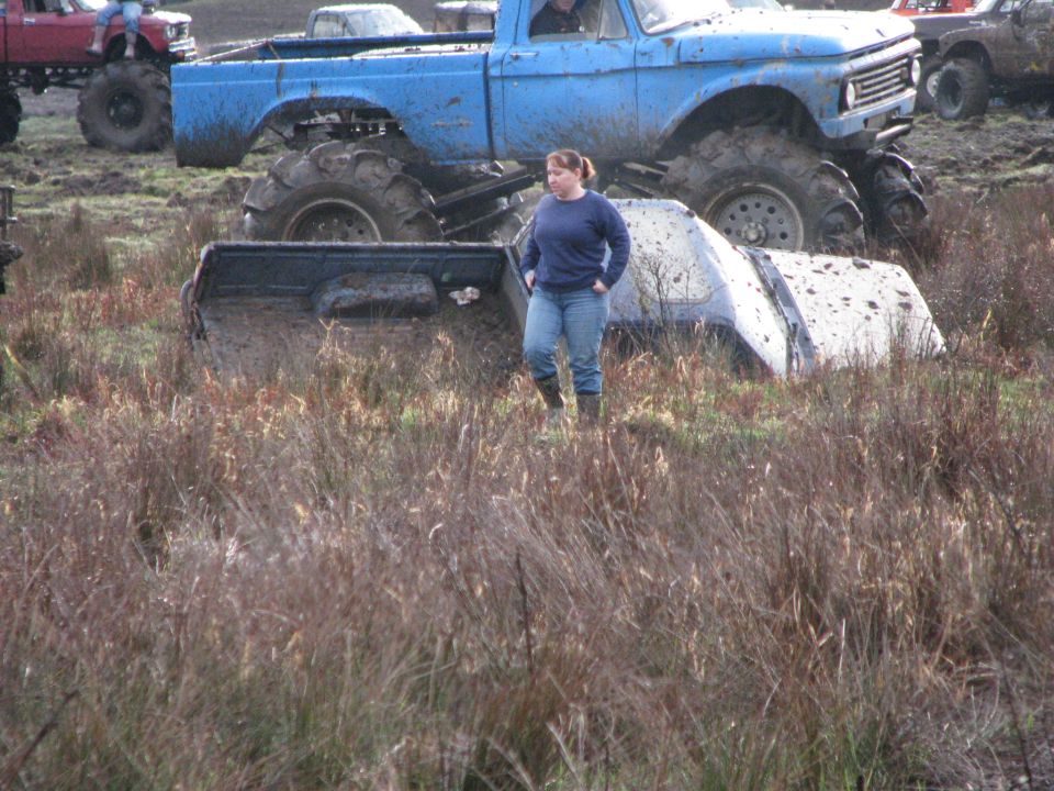 Mud bogging scene with a blue lifted truck and a white truck partially submerged in mud