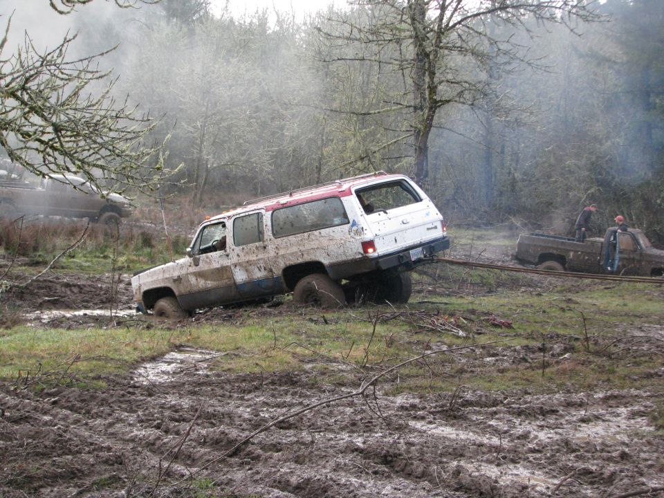 White SUV stuck in mud, being pulled by a brown pickup truck