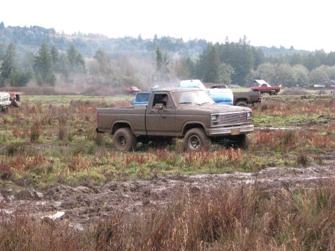 1978 Ford Bronco - A brown pickup truck navigates a muddy field with other vehicles in the background.
