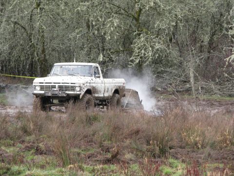1978 Ford Bronco - White pickup truck navigates a muddy off-road course with trees in the background.