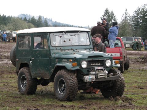 1978 Ford Bronco - A green Toyota Land Cruiser FJ40 is parked in a muddy field with other vehicles and people around.