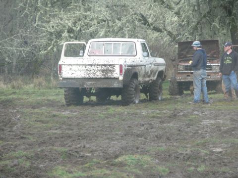 1978 Ford Bronco - Two muddy trucks sit in a field with people standing around them.