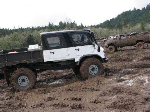 1978 Ford Bronco - Off-road vehicles navigate a muddy terrain, with one truck a snorkel and a flatbed.