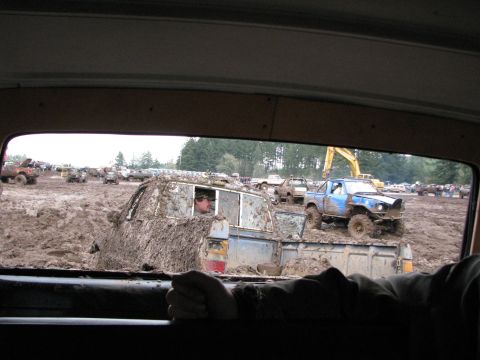 1978 Ford Bronco - Multiple off-road vehicles are stuck in deep mud at an event, with a yellow excavator in the background.