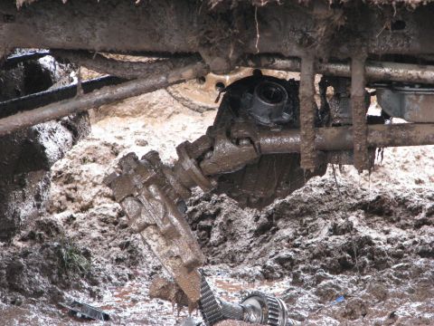1978 Ford Bronco - The vehicle's drivetrain components are heavily coated in mud, indicating it is stuck in a mire.