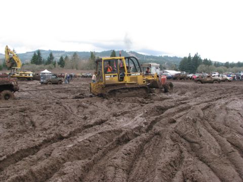 1978 Ford Bronco - A muddy field with a bulldozer and several other vehicles, suggesting an off-road event.