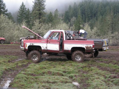 1978 Ford Bronco - Muddy off-road scene with a red and white pickup truck and another vehicle in the background.
