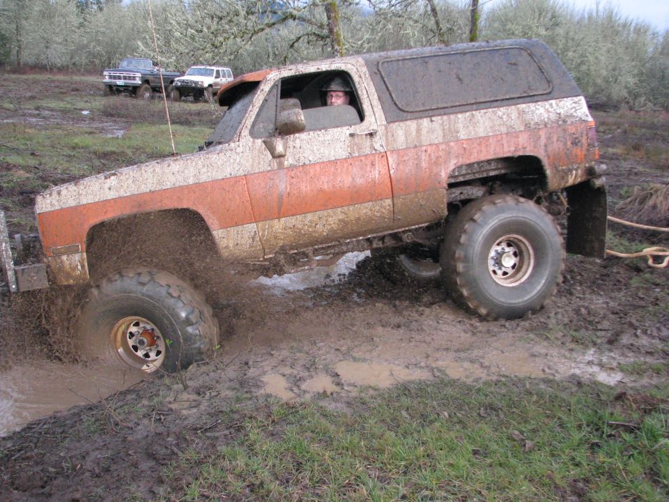 Mud-splattered off-road SUV with orange and white paint stuck in mud, other vehicles in background