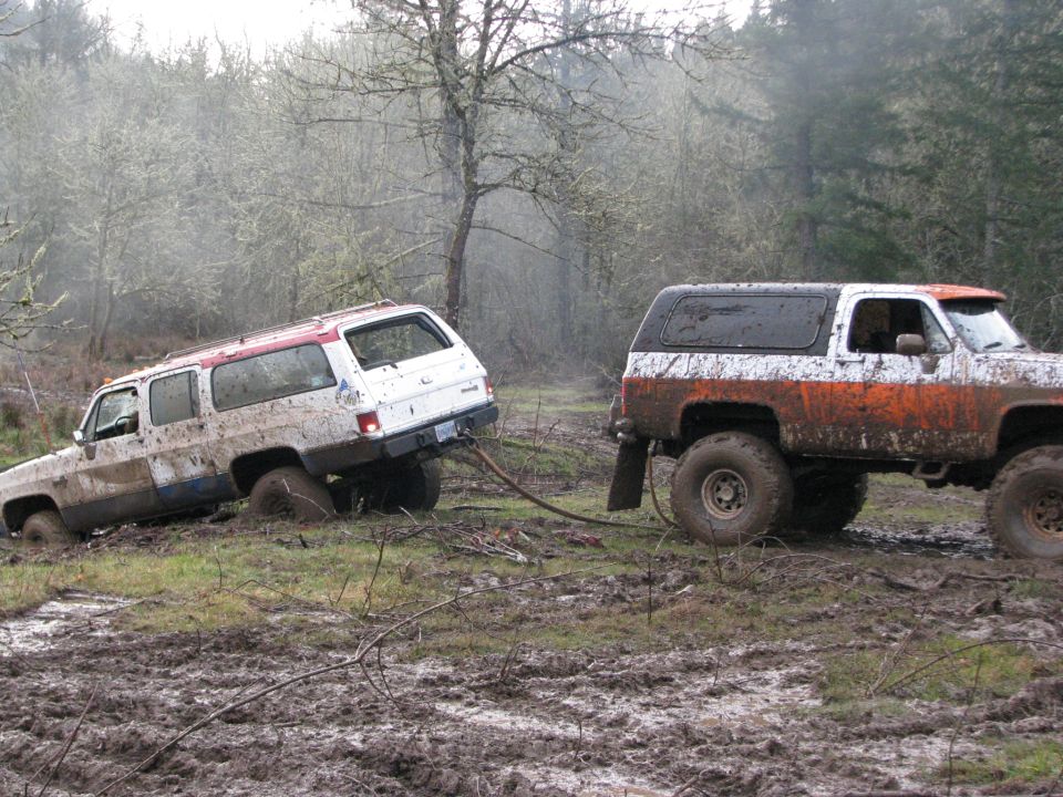 White SUV and orange/white SUV stuck in mud, being pulled by a tow strap