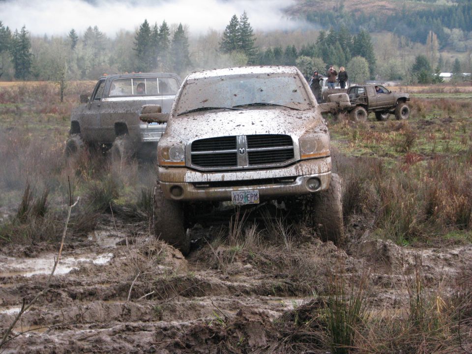 Pickup trucks driving through mud, one in foreground is a Dodge Ram