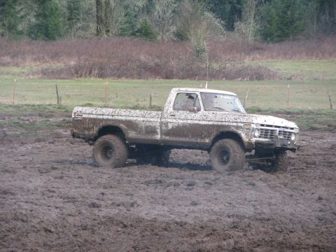 1978 Ford Bronco - A white pickup truck is stuck in the mud, its tires deep in the muck.