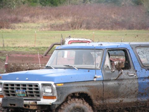 1978 Ford Bronco - Mud-covered 1978 Ford Bronco navigates a muddy terrain, with another vehicle visible in the background.