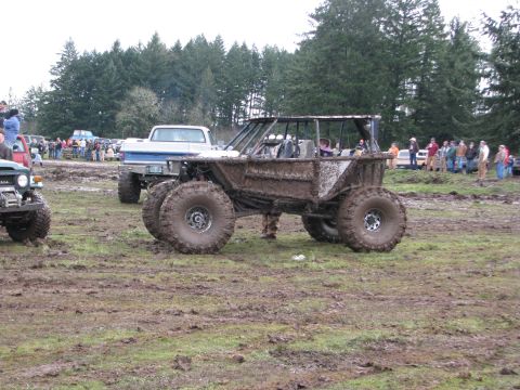1978 Ford Bronco - A heavily modified off-road vehicle sits covered in mud after an event, with spectators gathered in the background.