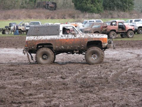 1978 Ford Bronco - This SUV is covered in mud as it navigates a muddy track, with other vehicles visible in the background.