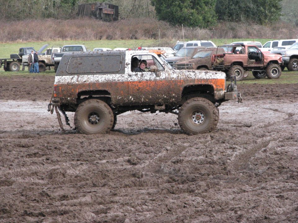 Mud-splattered white and orange SUV with large tires driving through mud