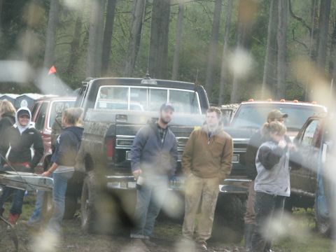 1978 Ford Bronco - Several people stand around a muddy black Ford F-Series truck in a wooded area.