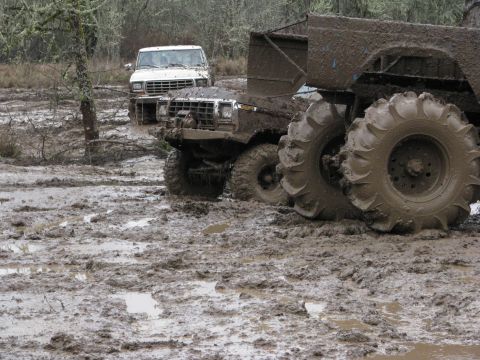 1978 Ford Bronco - Two off-road vehicles are stuck deep in the mud, with one prominently oversized tires.
