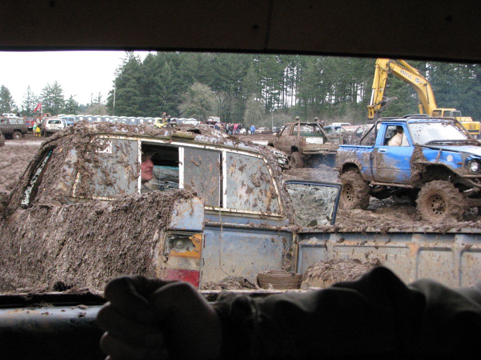Mud-covered vehicles in off-road event, blue pickup truck prominent