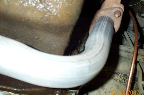 1986 Ford Bronco - Tight underbody view of a new aluminized exhaust down pipe curving away from a rusty cast exhaust manifold flange, routed past the oil pan…