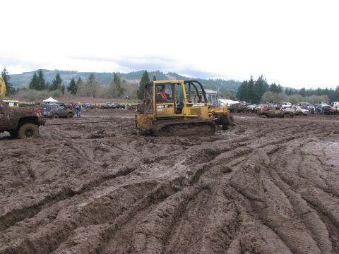 1978 Ford Bronco - A John Deere bulldozer navigates a muddy terrain, with several other vehicles visible in the distance.